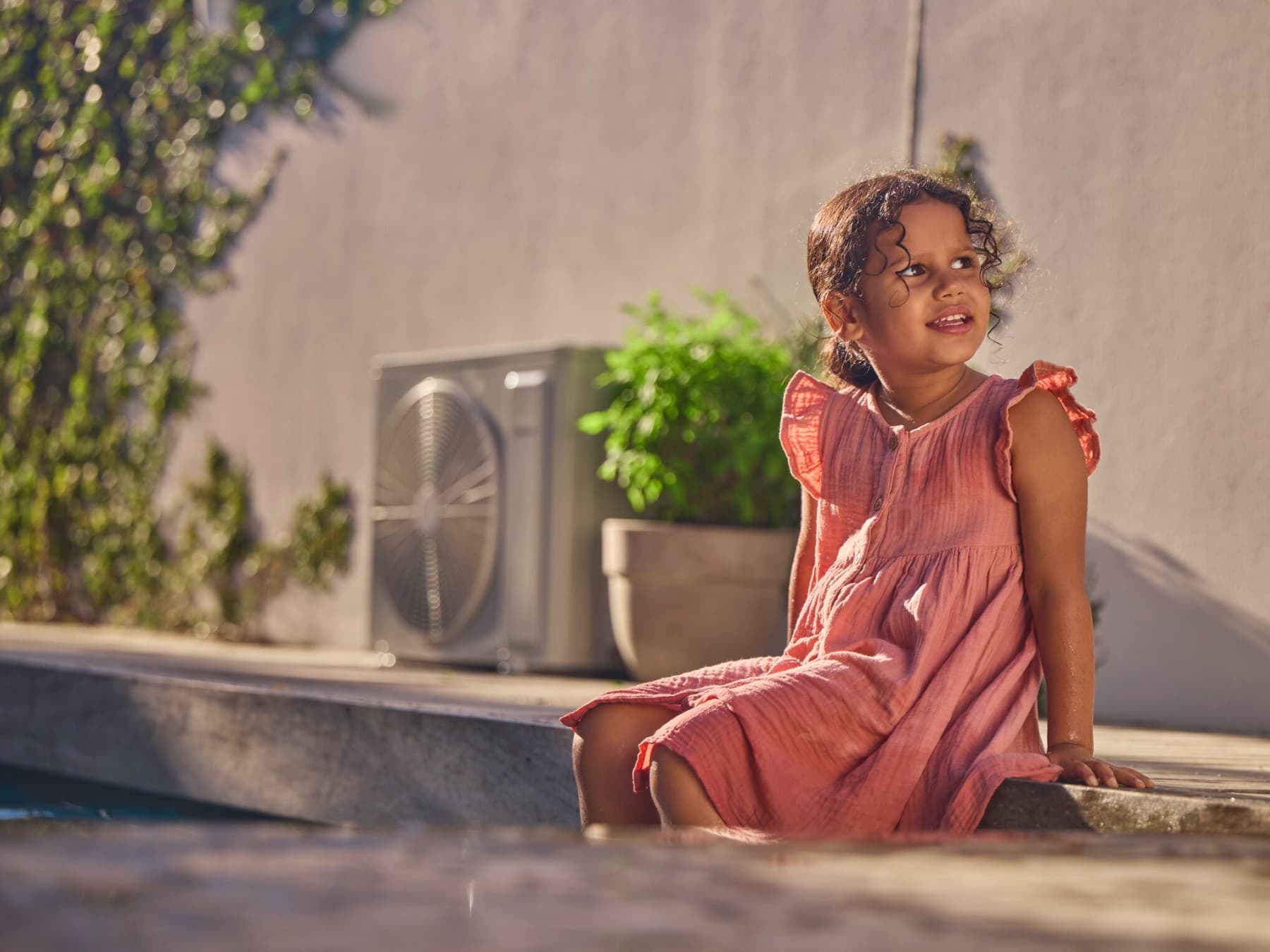 A girl sitting in the garden next to a heat pump