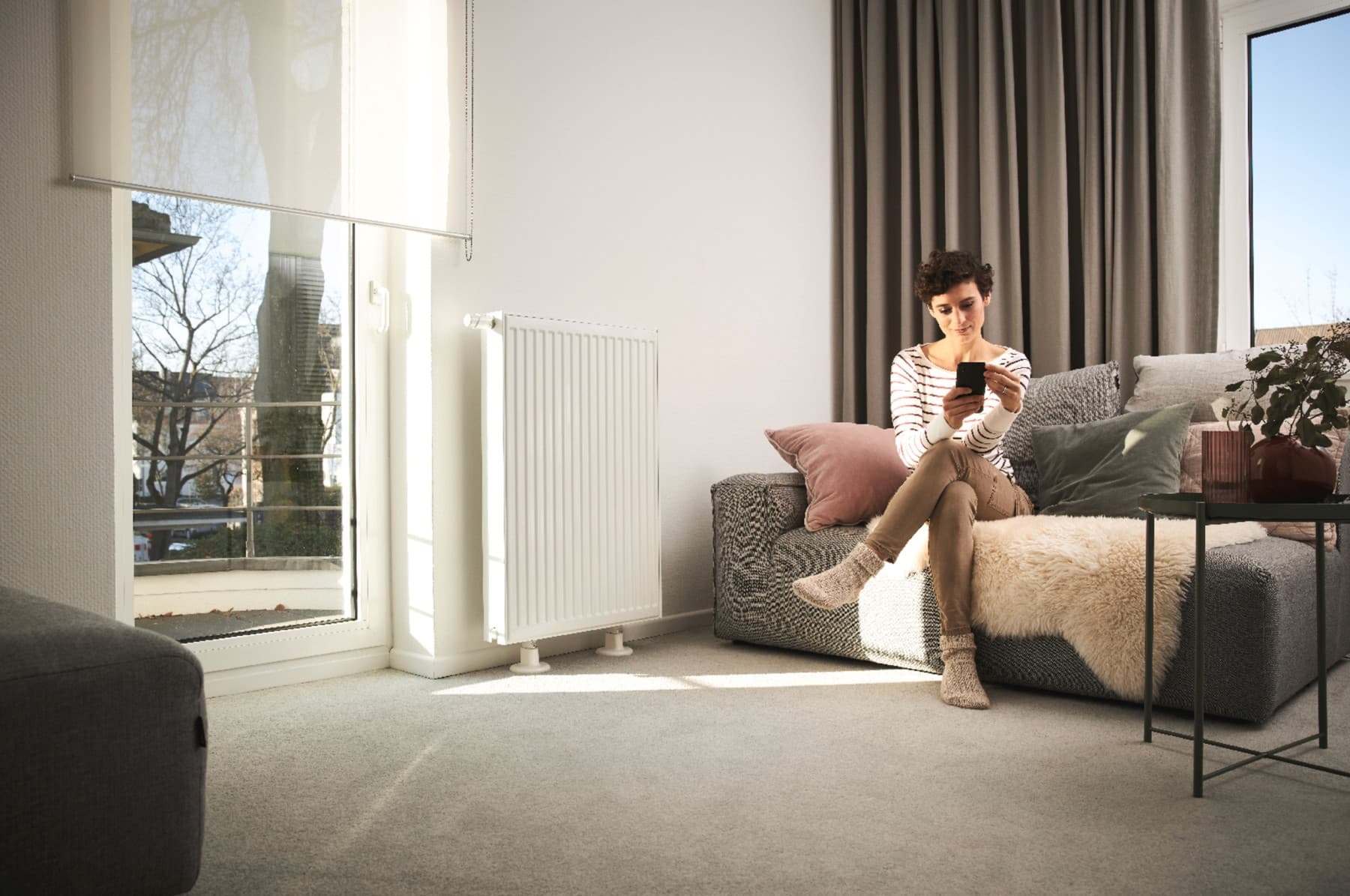 Woman sitting on sofa next to radiator looking at mobile phone