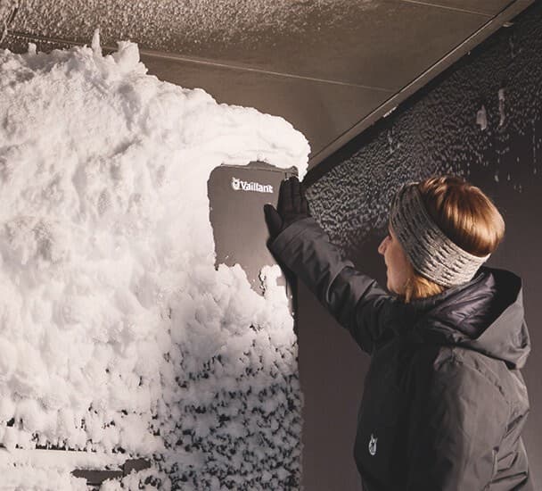 Woman removing ice from Vaillant logo on heat pump