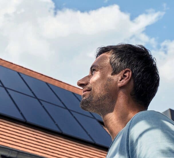 A man looking up at the sky. In the background, a roof fitted with photovoltaic panels can be seen