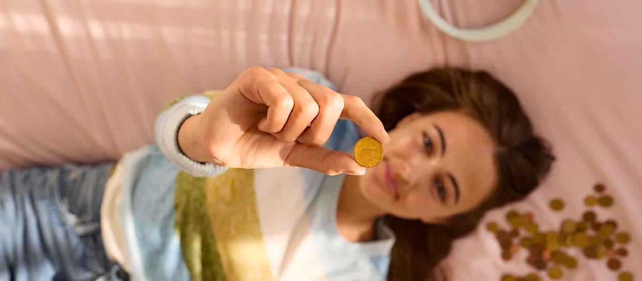 A girl is lying on a bed, holding up a coin