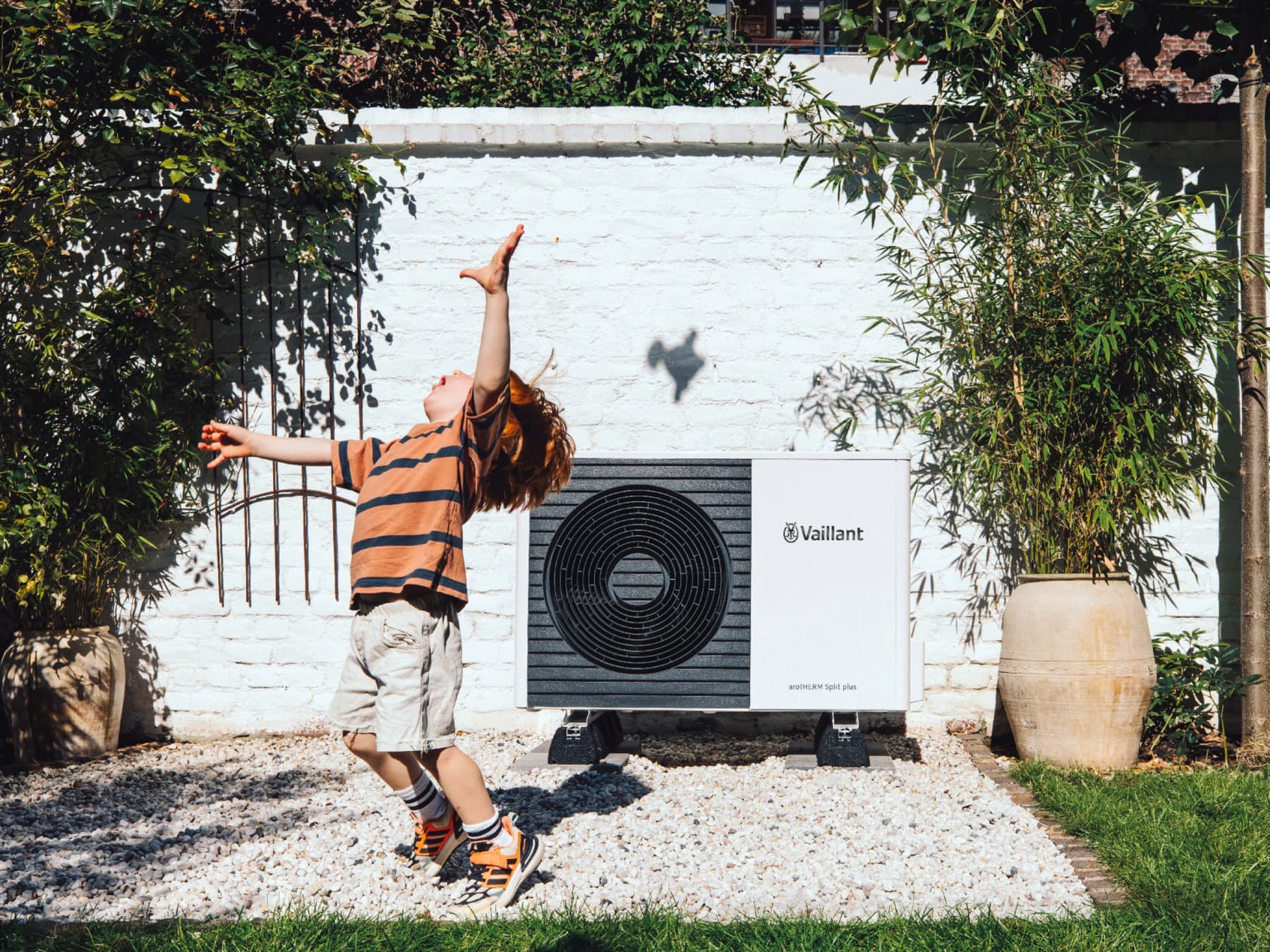 Child playing football in the garden infront of a heat pump