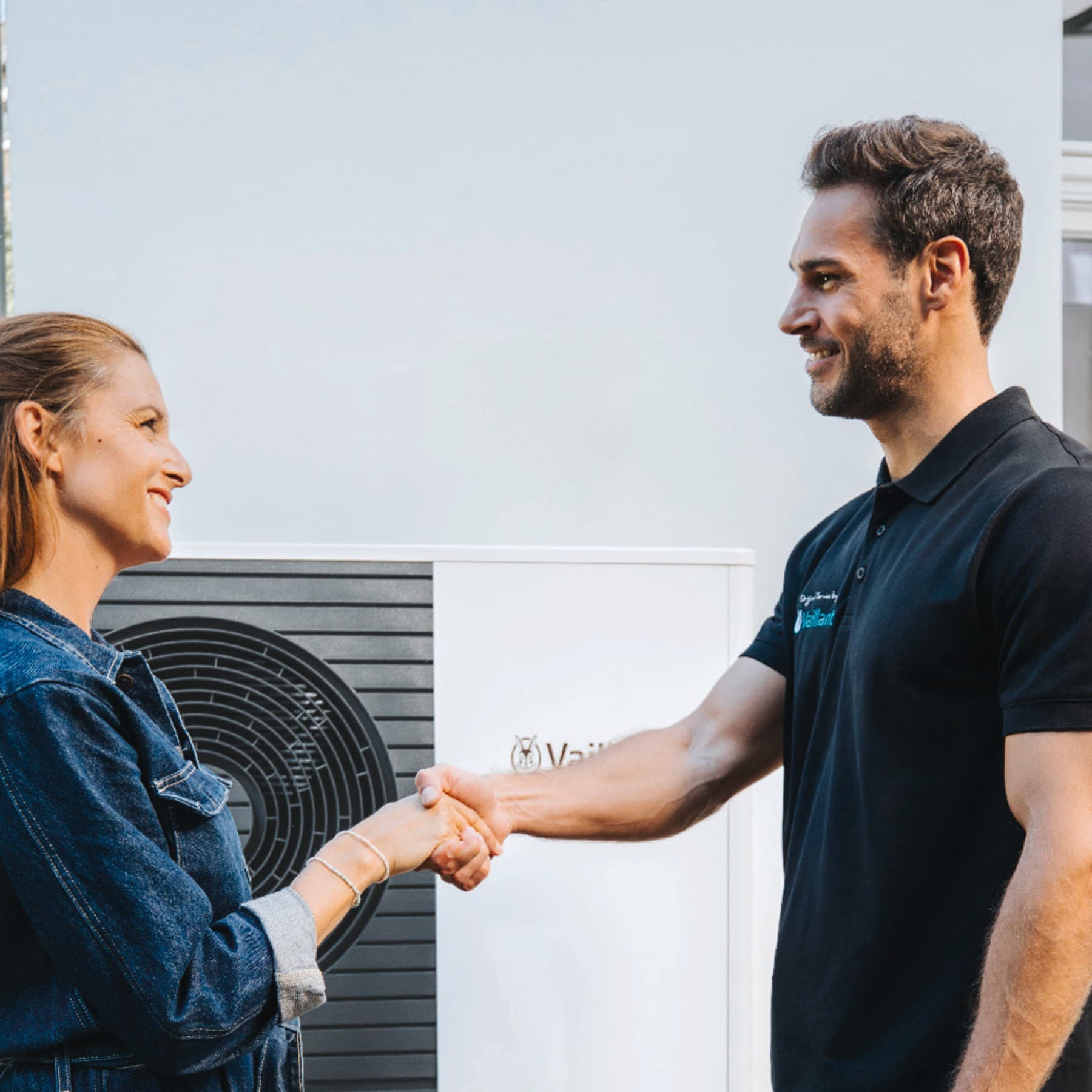 An installer and a woman shaknig hands in front of a heat pump