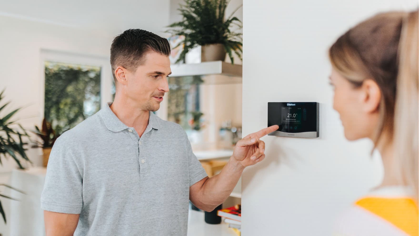 Un homme est au premier plan, la main posée sur un thermostat fixé à un mur bleu.