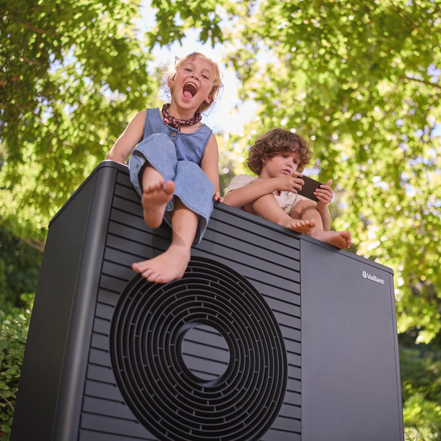 Deux enfants assis sur une pompe à chaleur Vaillant aroTHERM plus