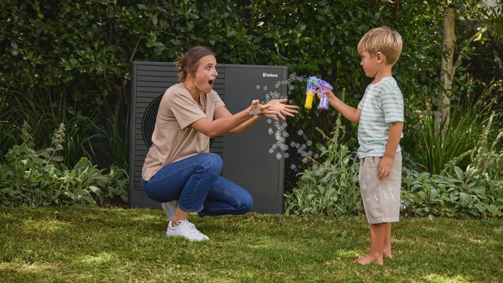 kid blowing bubbles in the garden with his mom and a heat pump in the background
