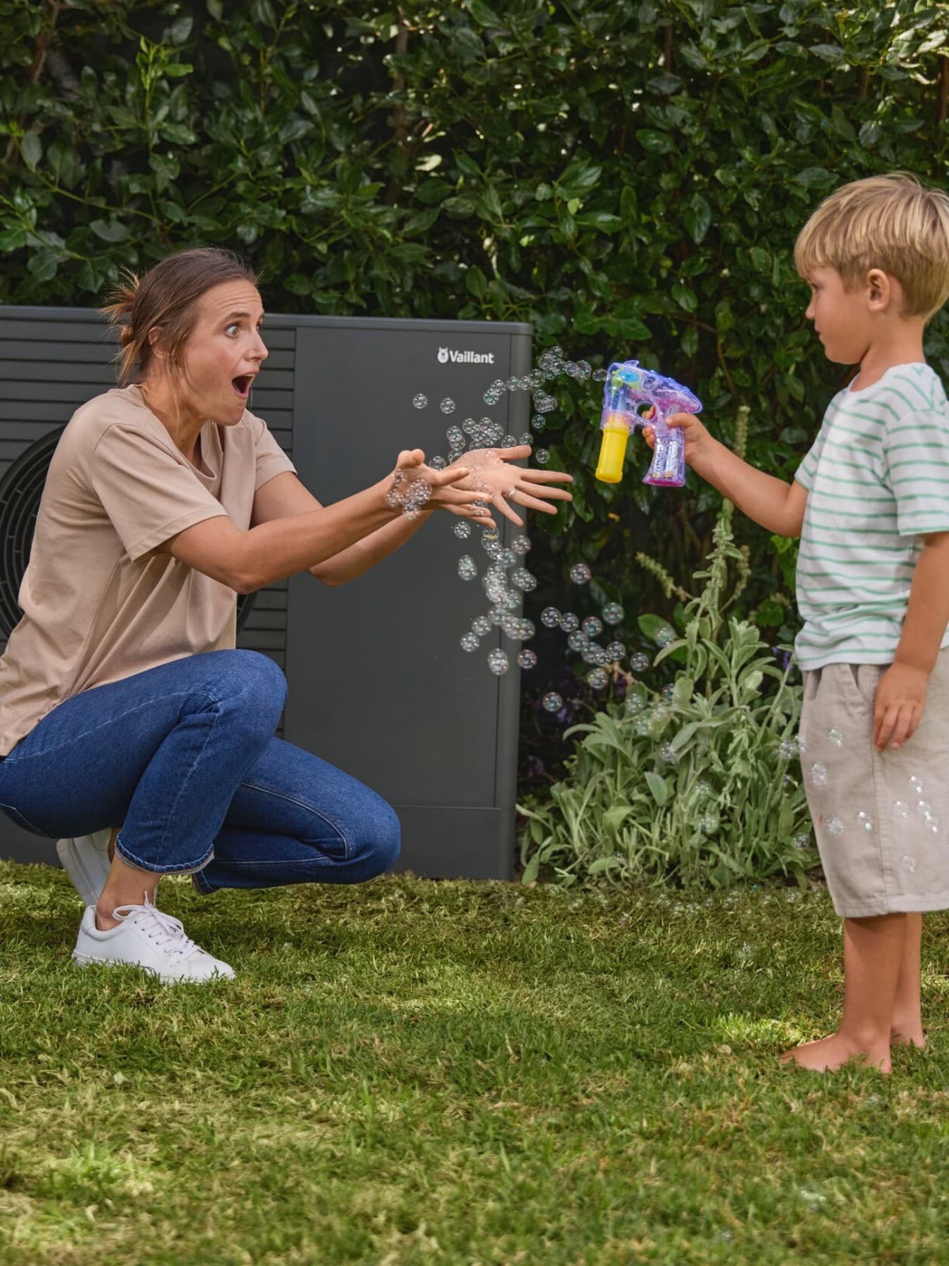 kid blowing bubbles in the garden with his mom and a heat pump in the background