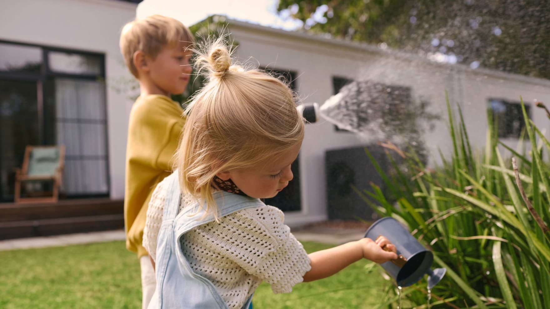 Children watering plants in a garden with a heat pump in the background
