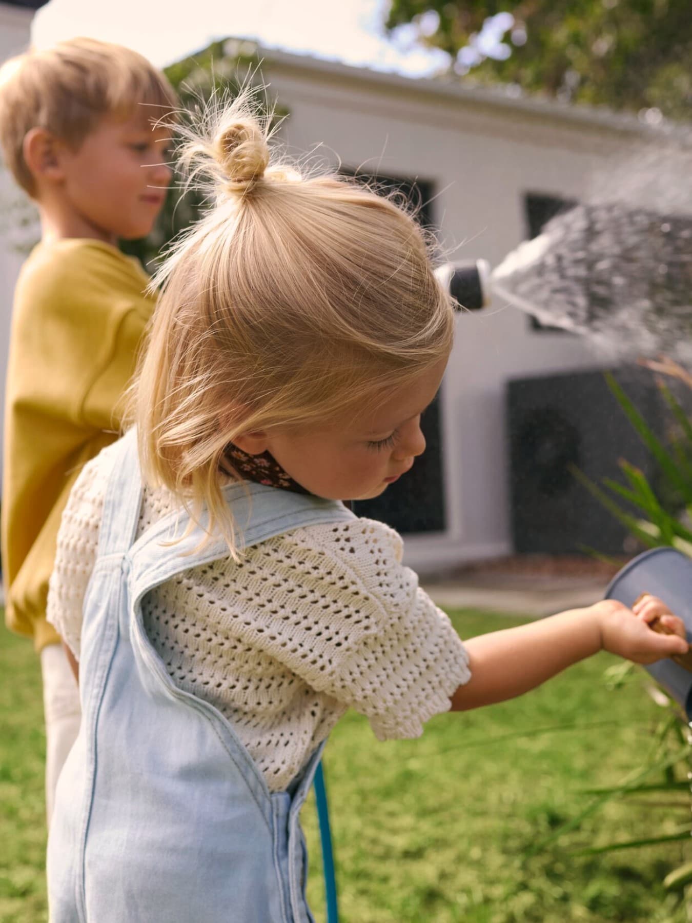 Children watering plants in a garden with a heat pump in the background