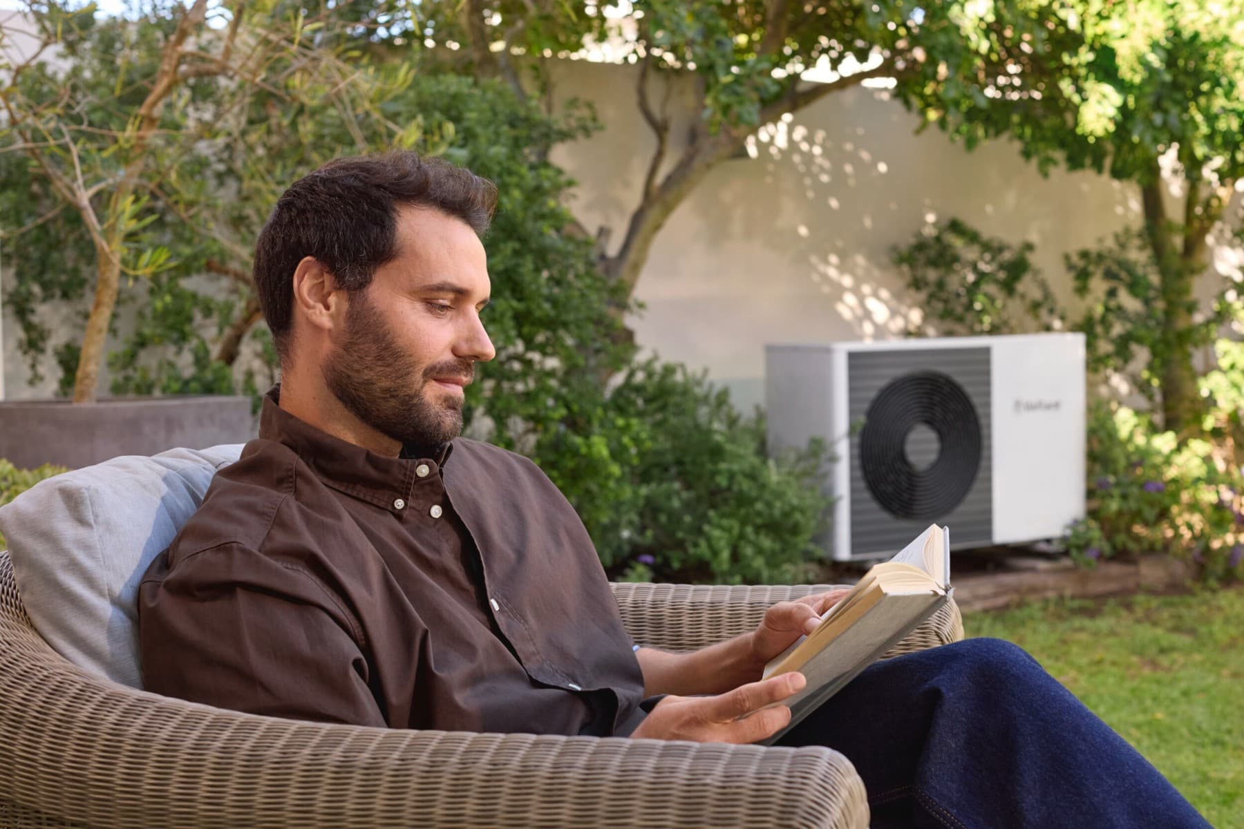 A man sitting in a garden in front of a heat pump