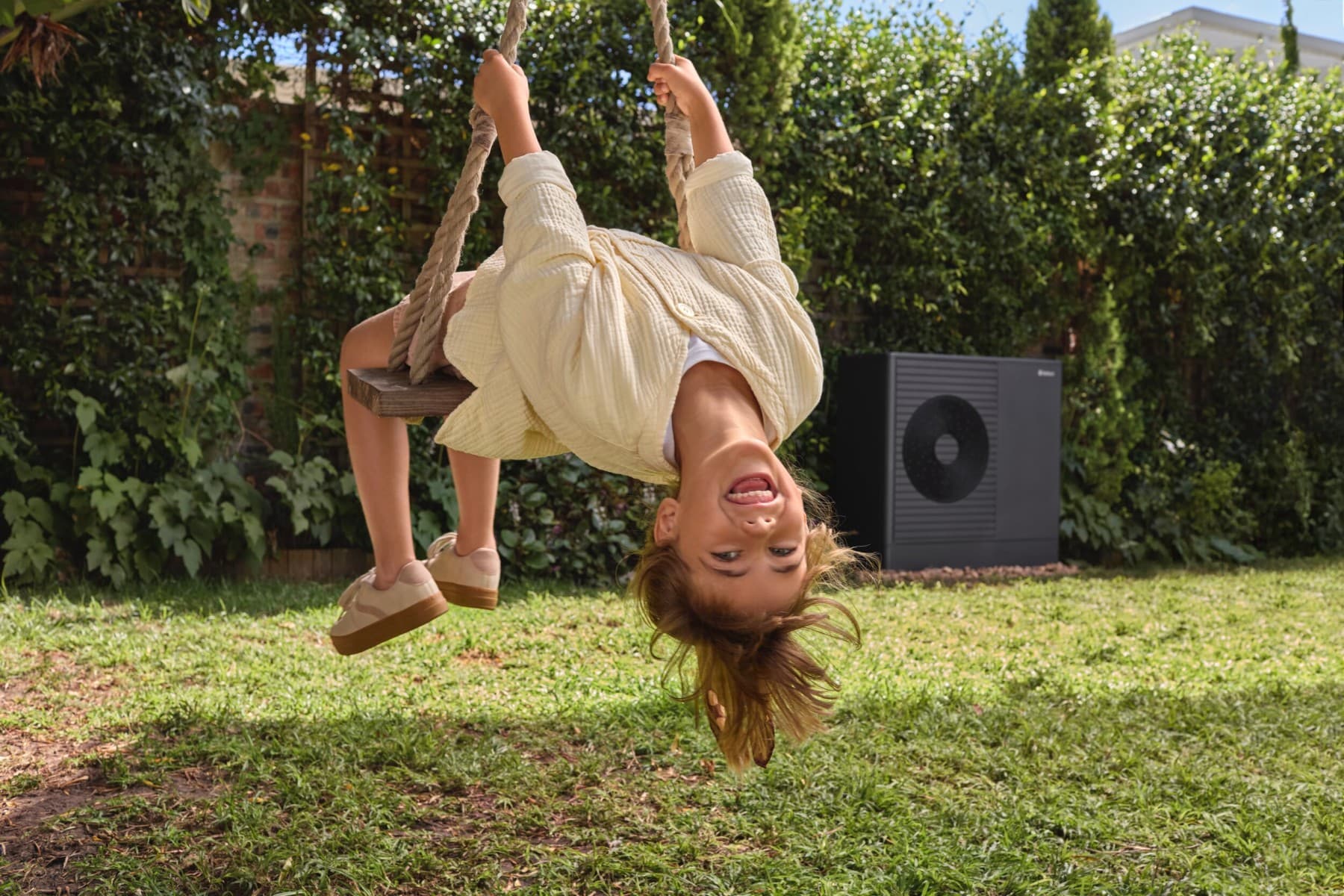 A child on a swing in the yard in front of a heat pump