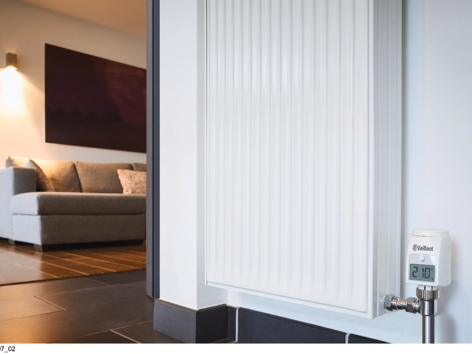 A radiator with a couch and cozy light in the background, the radiator's display shows 21°